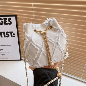 Chic white tweed bucket bag with gold chain strap and pearl accents shown in lifestyle setting