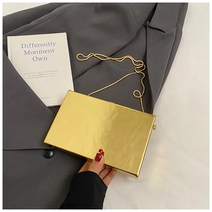 Close-up of golden rectangular acrylic clutch bag with metal snake chain on gray suit