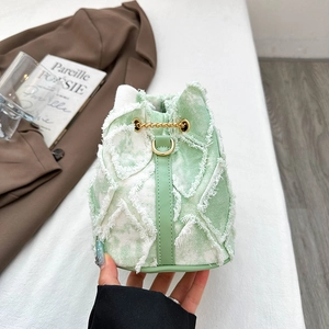 Detail view of denim bucket bag with frayed tassels and golden chain drawstring