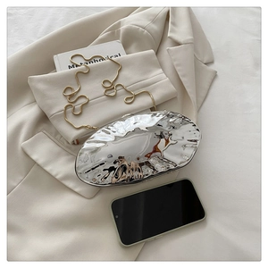 Mirror silver egg-shaped evening clutch bag with gold chain shown next to a smartphone