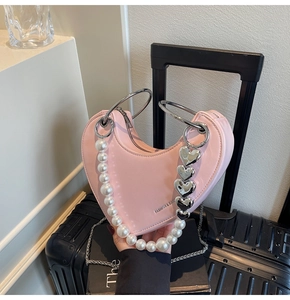 Dettaglio borsa cuore rosa con catena di perle e manico argento sopra valigia nera
