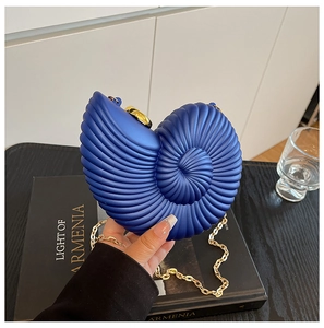 Detail of dark blue nautilus shaped acrylic clutch with gold chain held by a hand