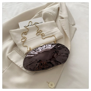 Close-up of a brown glossy oval clutch bag with a gold chain on a white blazer
