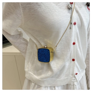 Close-up of mini gold metal crossbody bag with blue glitter panel on white dress