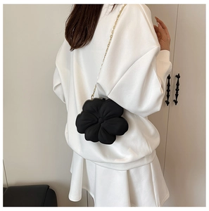 Detail of black flower evening bag with textured petals and golden chain strap on shoulder
