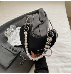 Dettaglio di borsa a mezzaluna nera con manici ad anello e ciondoli con perle e cuori