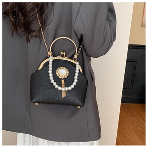Detail of retro black shell bag with pearl chain, gold handle and tassel on grey blazer