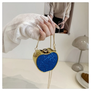 Macro view of blue glitter apple-shaped clutch bag with golden metal leaf clasp detail