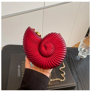 Deep red snail shell clutch with gold chain strap shown in a modern home setting