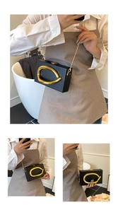 Macro detail of black matte box clutch with gold abstract ring hardware and chain