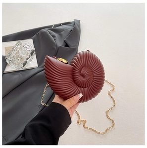 Macro shot of seashell-shaped acrylic clutch with burgundy spiral texture and gold chain