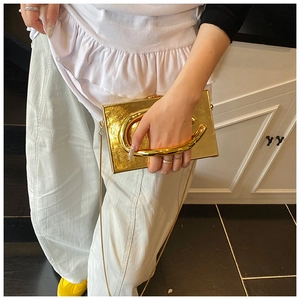 Detail of gold metallic box clutch with C-shaped handle and detachable chain strap