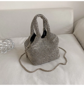 Detailed view of luxury silver rhinestone bucket bag with chain strap on a sofa