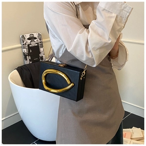 Detail of black acrylic box bag with golden sculptural metal handle and sleek chain