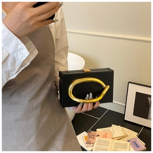 Detail of black acrylic evening clutch bag with chunky gold metal ring handle