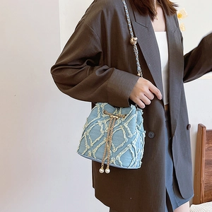 Detail of light blue denim bucket bag featuring quilted pattern and pearl drawstring