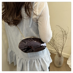 Detailed close-up of dark purple shell-shaped evening clutch with glossy ripple texture