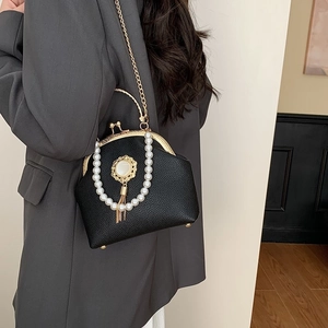 Black leather shell bag with pearl trim and gold tassel shown on a stylish model