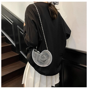 Detail of transparent acrylic snail shell bag with a slim metal chain strap on model