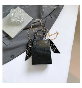 Detail of a shiny black rectangular handbag with a gold chain strap and silk scarf handle