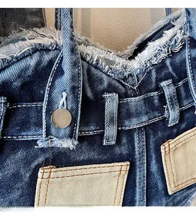 Detail of reinforced handle on distressed denim shoulder bag with metal buttons