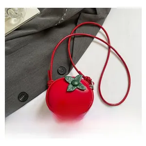 Détail d'un mini sac bandoulière rouge en forme de tomate avec feuilles vertes sur veste