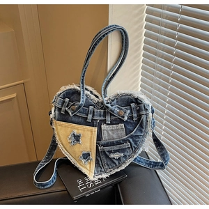 Detail of heart-shaped denim handbag with vintage frayed edges and star patch embroidery