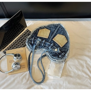 Detail of heart-shaped denim shoulder bag with raw edges and contrasting front pockets