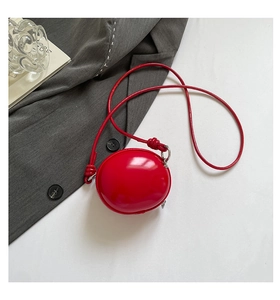 Détail du sac pomme en cuir verni rouge avec bandoulière nouée et finitions argentées