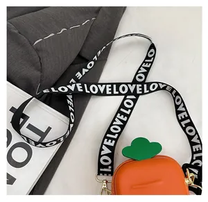 Detail of carrot-themed orange crossbody bag with green leaf and LOVE printed strap
