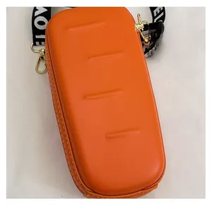 Detail of orange textured hardshell crossbody bag with stylish printed wide strap