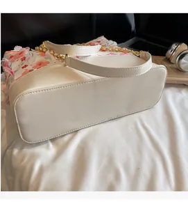 Détail du sac seau en cuir blanc avec imprimé floral rose et bandoulière chaîne dorée