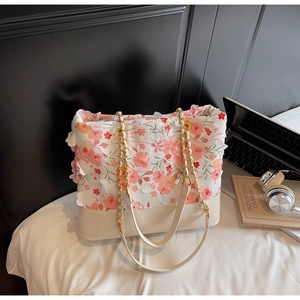 Détail de broderie florale et pétales 3D sur un sac seau en dentelle blanche à chaîne