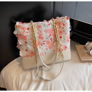 Détail du sac cabas floral avec pétales en tissu 3D et chaînes dorées sur tissu blanc