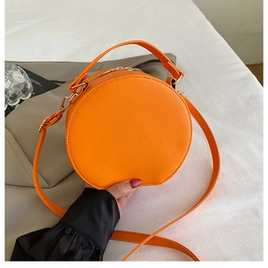 Détail du sac à bandoulière rond orange vif avec poignée et fermeture éclair dorée