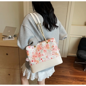 Détail d'un sac cabas blanc orné de fleurs 3D et d'une bandoulière en chaîne dorée