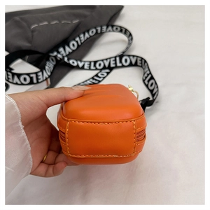 Close-up of orange textured PU leather crossbody bag with lettered strap and zip layers