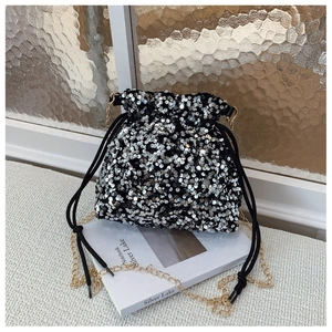 Detail of a black sequin drawstring bucket bag with a gold metal chain strap on a magazine