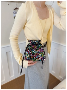 Detail of colorful sequin drawstring bucket bag with gold chain strap on female model