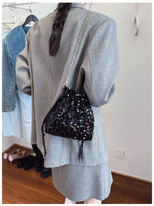 Detail of a black sequin bucket bag featuring a drawstring closure and gold chain strap