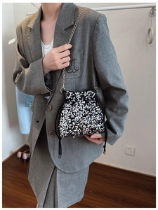 Detail of sequin drawstring bucket bag with gold chain strap on a grey suit outfit