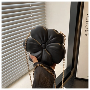Detail view of a 3D black flower evening bag with a thin gold metal chain strap