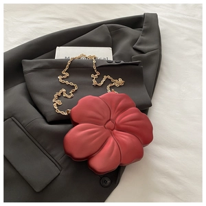 Detail of red flower-shaped clutch bag with matte texture and gold metal chain strap