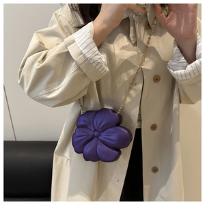 Detail of a purple flower-shaped crossbody bag with a slim gold chain on a trench coat
