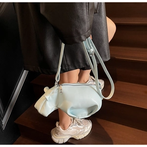 Sac bandoulière hippo bleu clair porté par un mannequin sur un escalier en bois