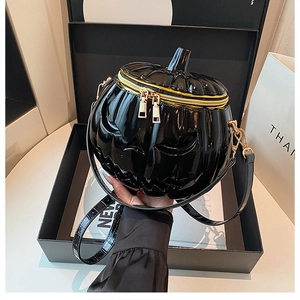 Detail of glossy black pumpkin-shaped handbag with golden double zipper and embossed face