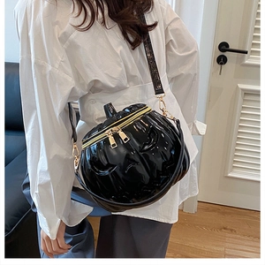 Detail view of glossy black pumpkin-shaped bag with gold-tone zippers and leather strap