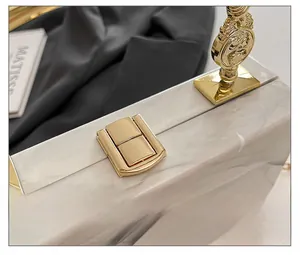 Detailed close-up of golden metal clasp on white marble texture acrylic evening clutch