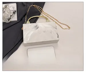 Detail of marble acrylic clutch with gold chain next to a smartphone for size reference