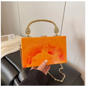 Detail of acrylic box clutch with orange marble texture and gold round metal handle